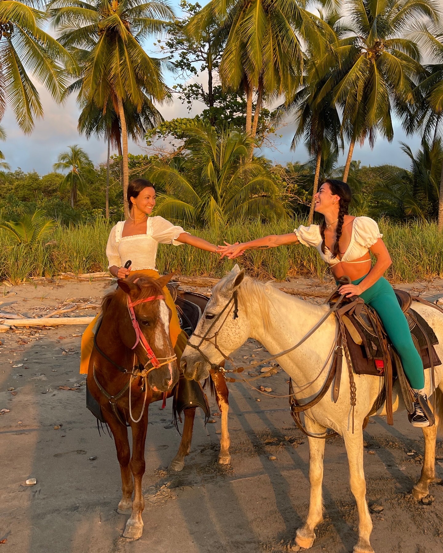 Two women horseback riding on the beach at sunset